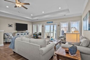 A spacious living room with a ceiling fan, a flat-screen TV, a sofa, a coffee table, and a view of the beach. - Beach Badger #147 - Rate Reduction! Ocean View Private Hot Tub, Dog Friendly! (North Topsail Beach)