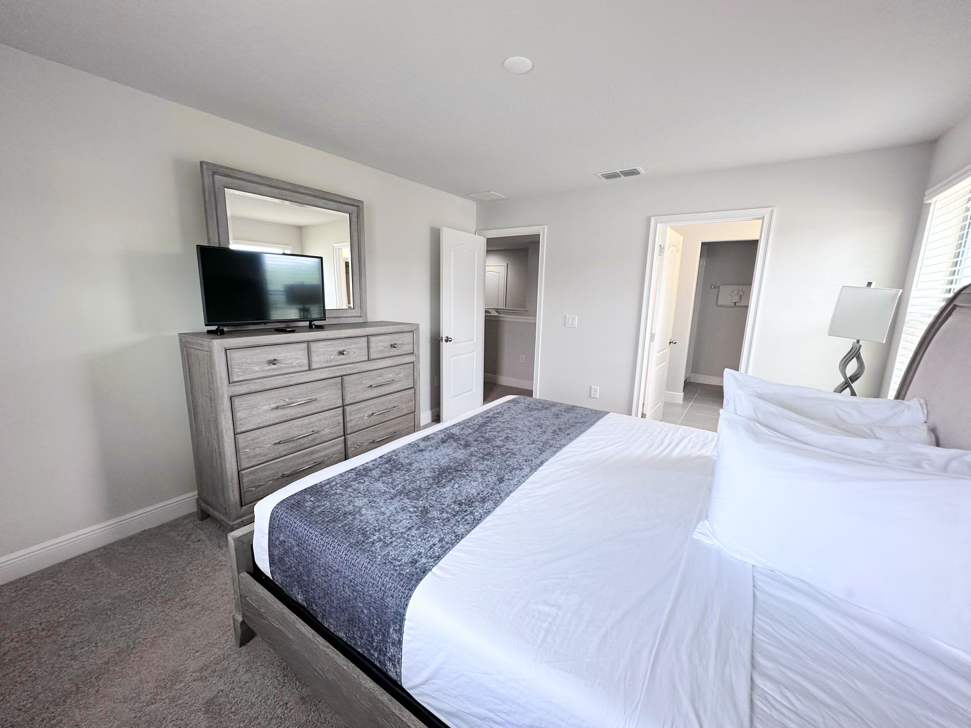 Une chambre à coucher avec un lit, une commode, un téléviseur posé sur la commode et une porte donnant sur une autre pièce.