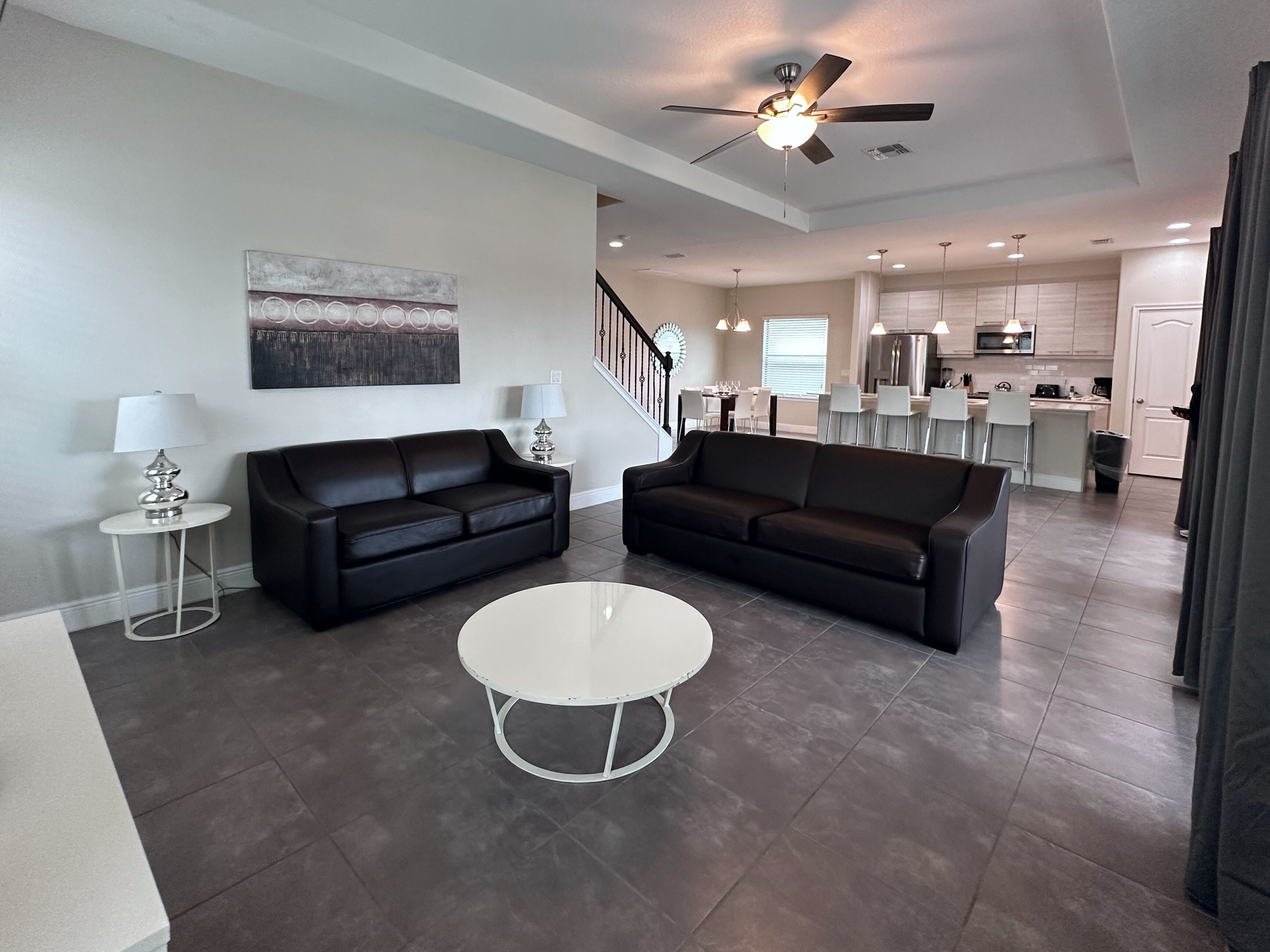 A modern living room with two black leather sofas, a white coffee table, and a ceiling fan.