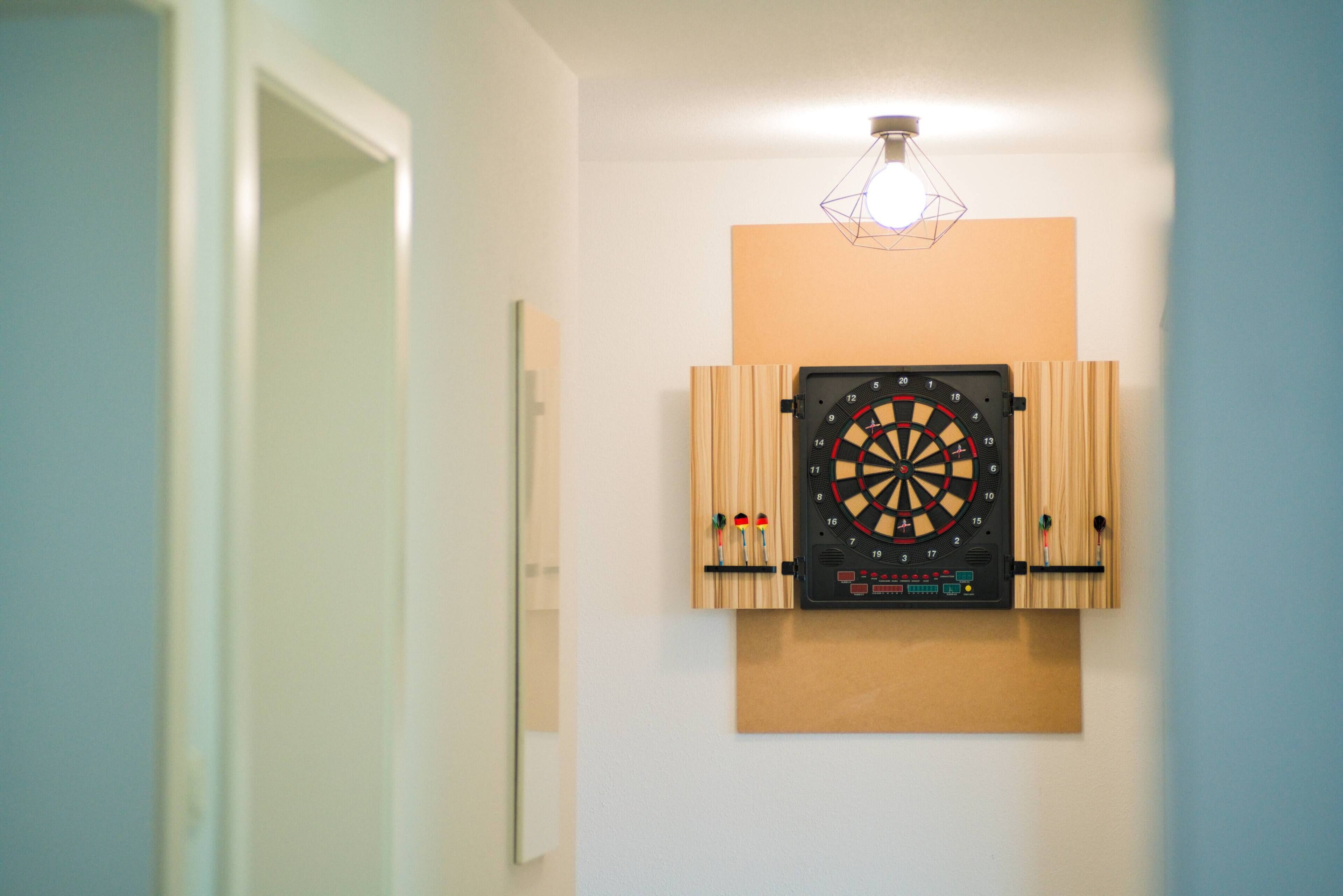 Eine Dartscheibe an einer Wand, darüber eine Deckenleuchte.