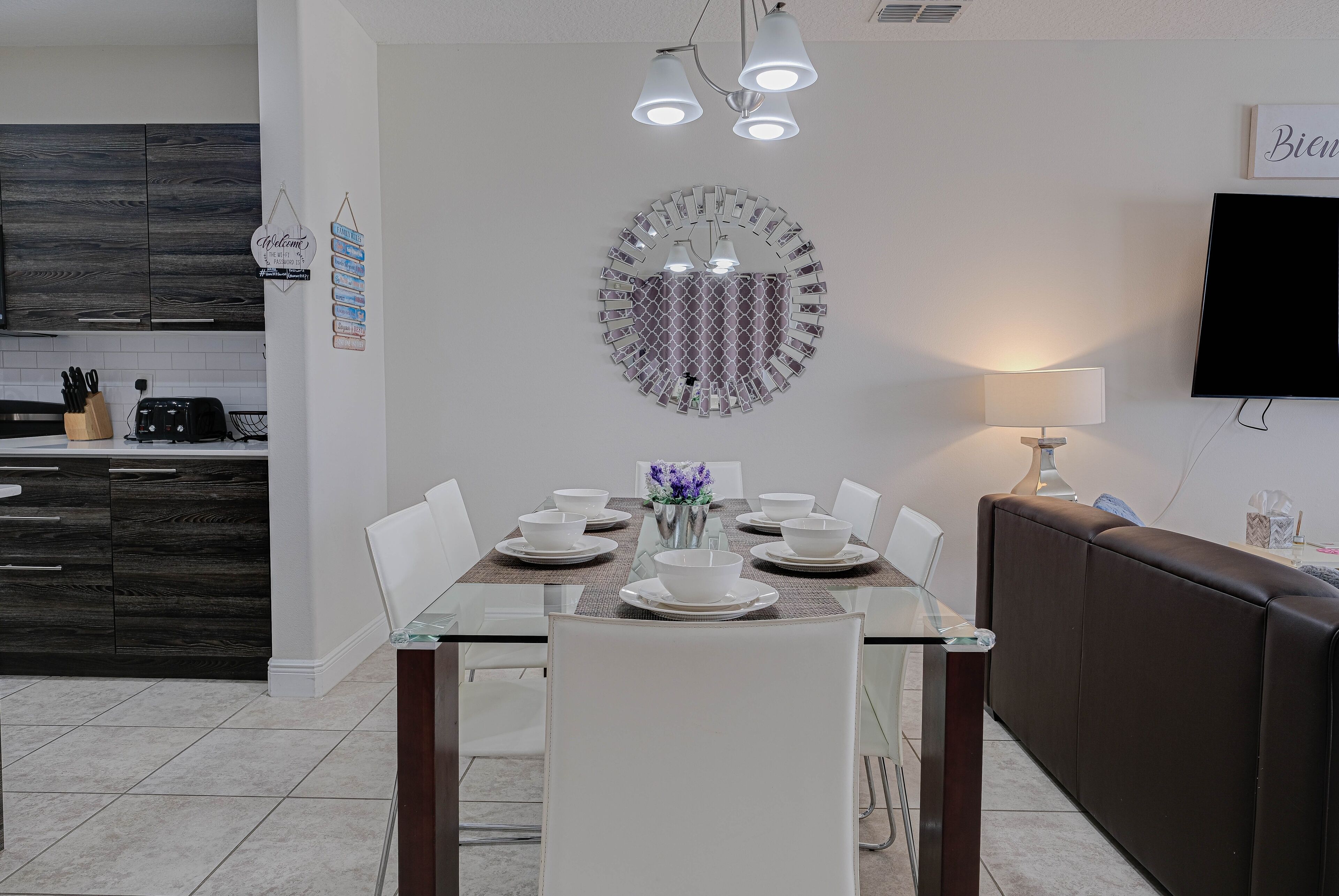 Un comedor moderno con una mesa de vidrio, sillas blancas y un espejo decorativo en la pared.