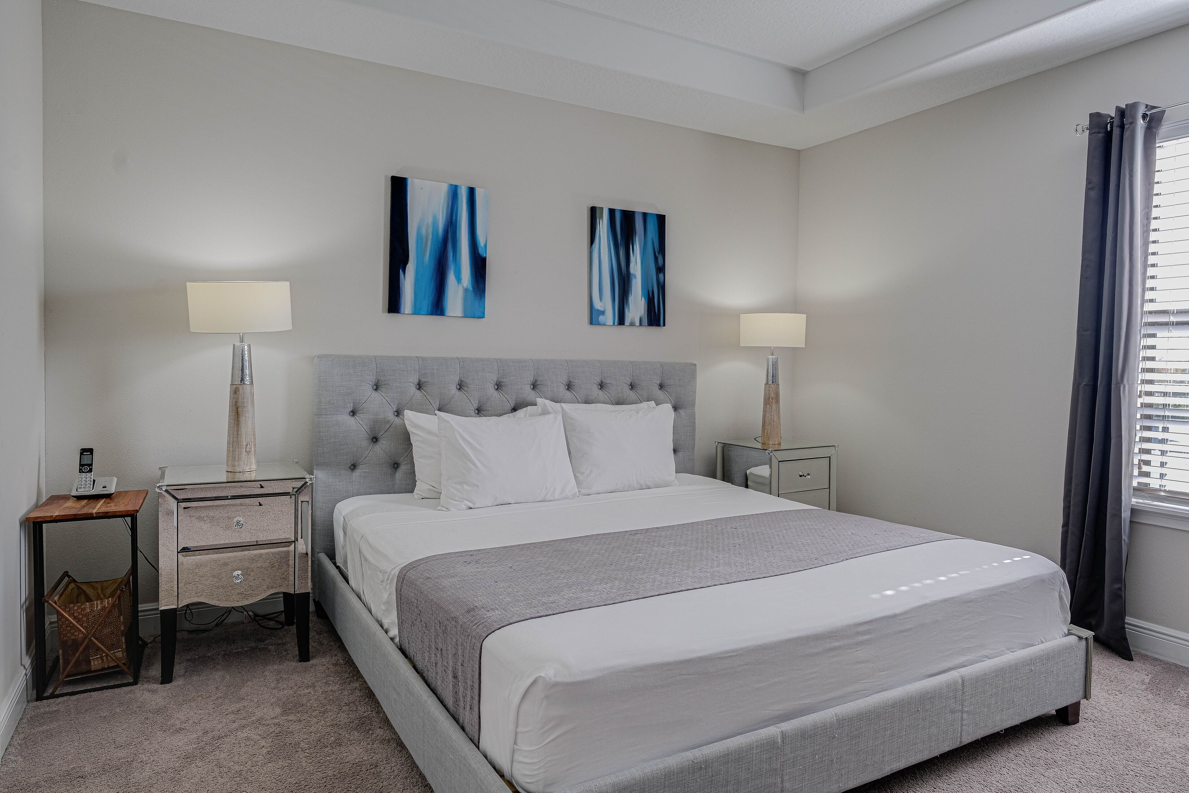 Une chambre à coucher bien aménagée, avec un grand lit, deux tables de chevet, une lampe de chevet et des œuvres d’art abstraites accrochées au mur.