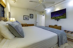 Une chambre d’hôtel avec un lit, un téléviseur fixé au mur, un ventilateur de plafond et une porte donnant sur une autre pièce.
