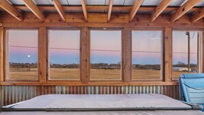 Una habitación con una cama grande, vistas por varias ventanas y techo de madera.