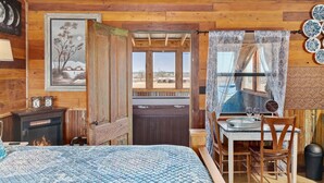 Una habitación de cabaña rústica con una cama, una mesa con sillas, chimenea y vistas al exterior.