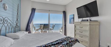 A bedroom with a bed, a television, a dresser, and a balcony with a view of the ocean.