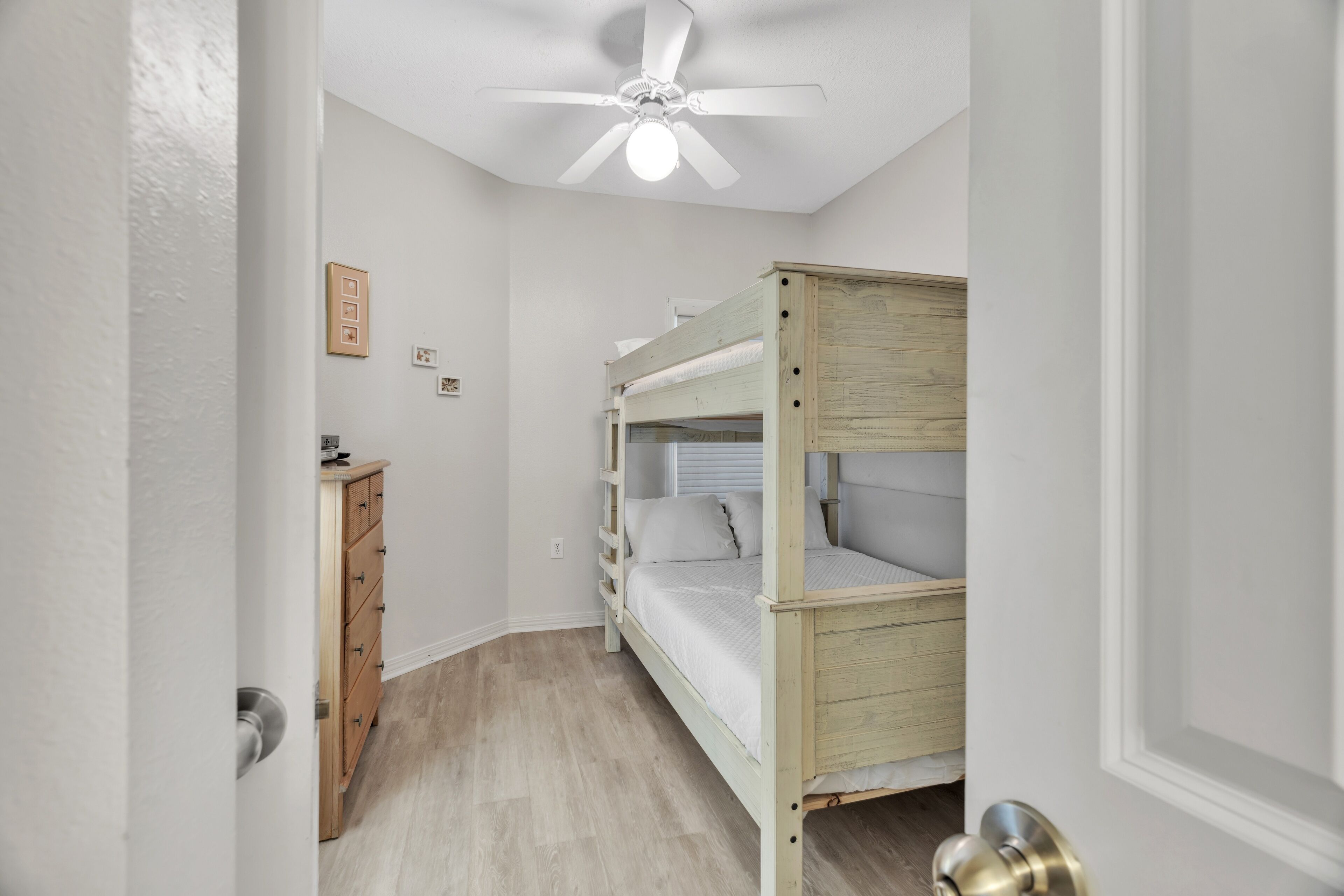 Ein Schlafzimmer mit Etagenbett, einem Holzkapuzenpaneel, einem Deckenventilator und einer Tür mit silberner Klinke.