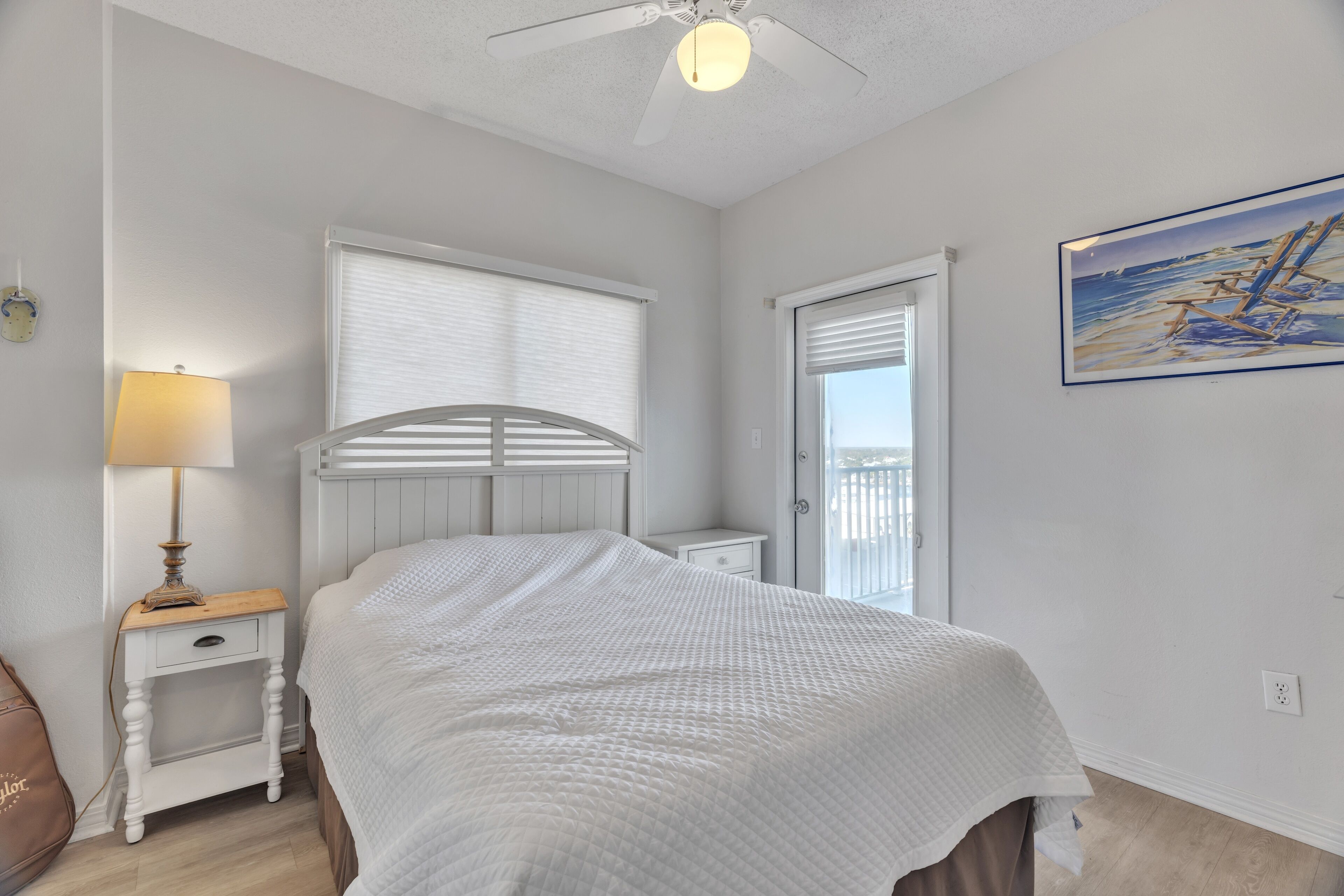A bedroom with a bed, a nightstand, a lamp, a ceiling fan, and a window with blinds.
