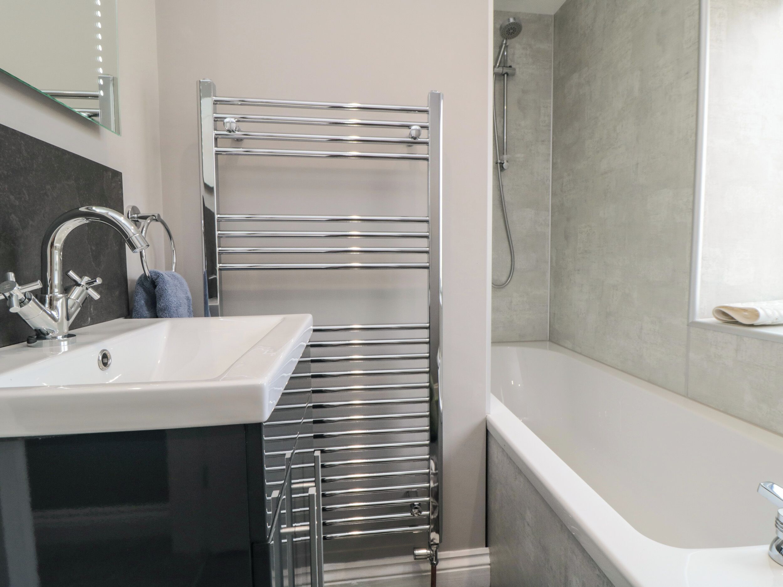 A modern bathroom with a white sink, chrome fixtures, a glass shower enclosure, and a towel rack.