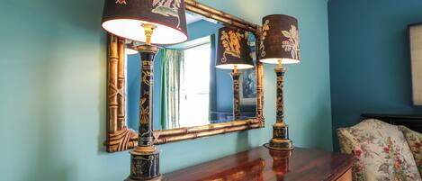 Een kamer met een houten dressoir, twee sierlijke lampen en een spiegel die de kamer weerspiegelt.