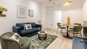 Un salon moderne avec un canapé bleu, un fauteuil vert et un coin repas comprenant une table et des chaises en bois.