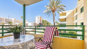 A balcony with a table, chair, potted plant, and a view of buildings and palm trees.