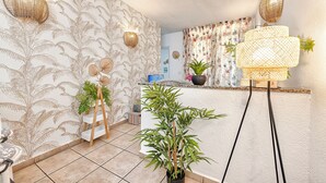 A room with a patterned wallpaper, a wooden easel, a potted plant, a floor lamp, and a television.