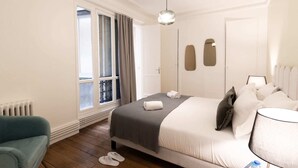 Een hotelkamer met een bed, een stoel, een radiator, een raam met gordijnen en een hanglamp.