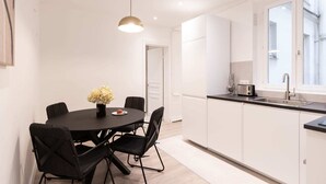 Een moderne keuken met witte kasten, een zwart aanrecht en een ronde eettafel met vier stoelen.