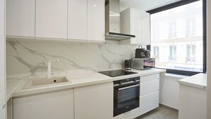 A modern kitchen with white cabinets, a marble countertop, a built-in oven, and a window with a view of buildings. - Sublime 3 bedrooms flat center of Paris Montmartre (Paris)