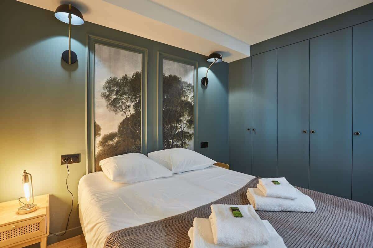 A bedroom with a bed, two bedside lamps, a nightstand, and a wardrobe.