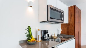 A modern kitchen with a microwave, coffee maker, and a bowl of fruit on the counter.