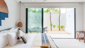 A modern bedroom with a bed, a ceiling fan, a view of a patio with plants and a table.