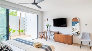 A modern bedroom with a bed, desk, chair, TV, and a balcony with plants.