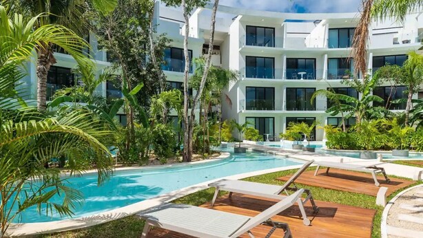 A modern hotel with a pool area, surrounded by lush greenery and palm trees.