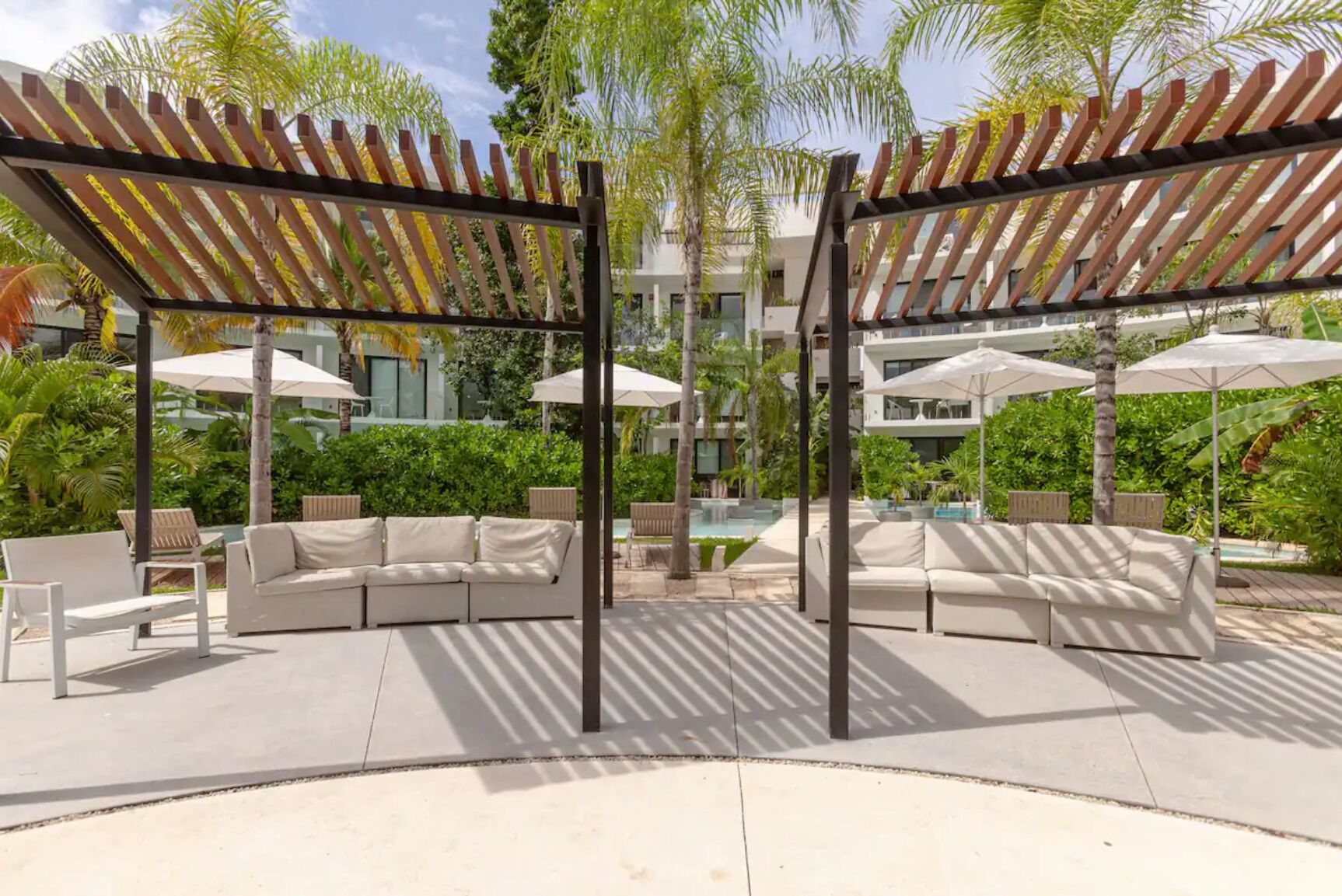 A poolside area with a covered seating area, umbrellas, and a pool.