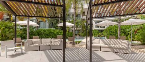 A poolside area with a covered seating area, umbrellas, and a pool.