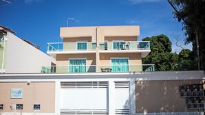 A multi-story building with a flat roof, large windows, and a balcony with outdoor furniture. - Casa Super Moderna (Cabo Frio)