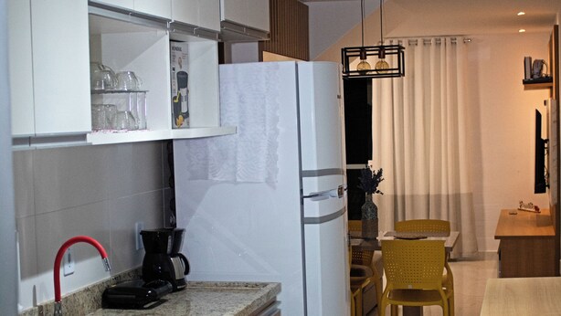 A compact kitchen with a sink, countertop, and a refrigerator. There is a dining area with a table and chairs. - Casa Super Moderna (Cabo Frio)