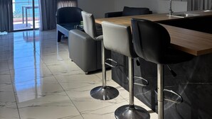 A modern kitchen with a wooden countertop, black bar stools, and a view of the sea through large windows. - Hotel San Diego (Kfar Yassine)