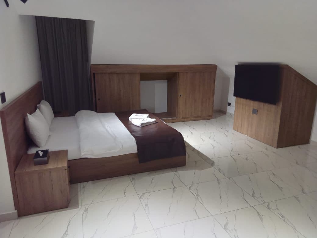 A hotel room with a bed, a nightstand, a wooden wardrobe, and a built-in bench.