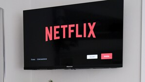 A flat-screen TV mounted on a wall displaying the Netflix logo, a pink vase with flowers, a small potted plant, and a white radiator below. - Cozy modern studio apartment – perfect for couples (Pieve A Nievole)