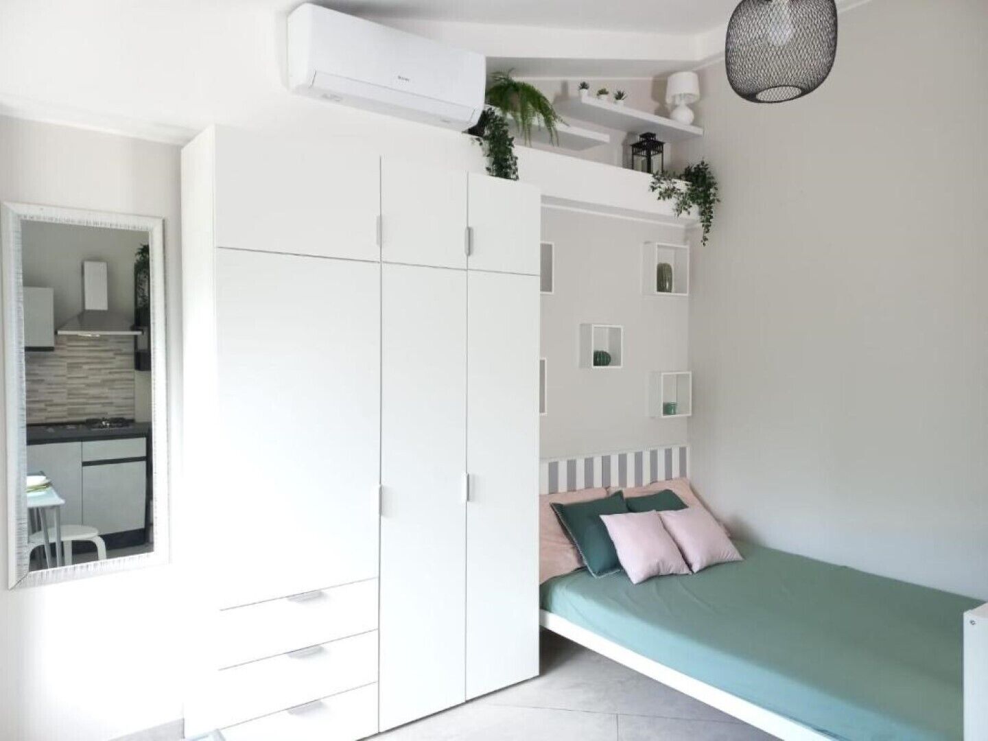 Ein Schlafzimmer mit Bett, Kleiderschrank, Spiegel und einer kleinen Küchenzeile.