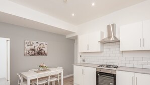 A modern kitchen with white cabinetry, a gas stove, and an oven. There is a dining table with chairs and a wall-mounted artwork.