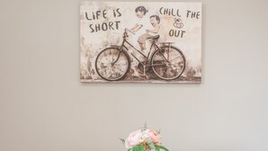 A dining table with a wall art depicting a bicycle and motivational text, and a vase with flowers on a tray.