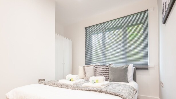 A modern bedroom with a bed, a wardrobe, and a window with blinds.