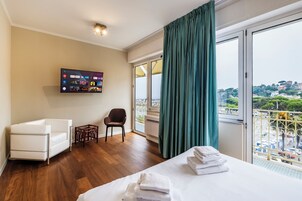 Habitación de hotel con cama, una silla, televisor montado en la pared y balcón con vista a la ciudad.