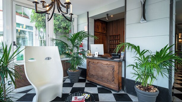 A reception area with a modern desk, a white chair, and potted plants. - Rosabianca Boutique Hotel (Rapallo)