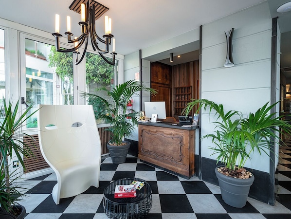 A reception area with a modern desk, a white chair, and potted plants. - Rosabianca Boutique Hotel (Rapallo)