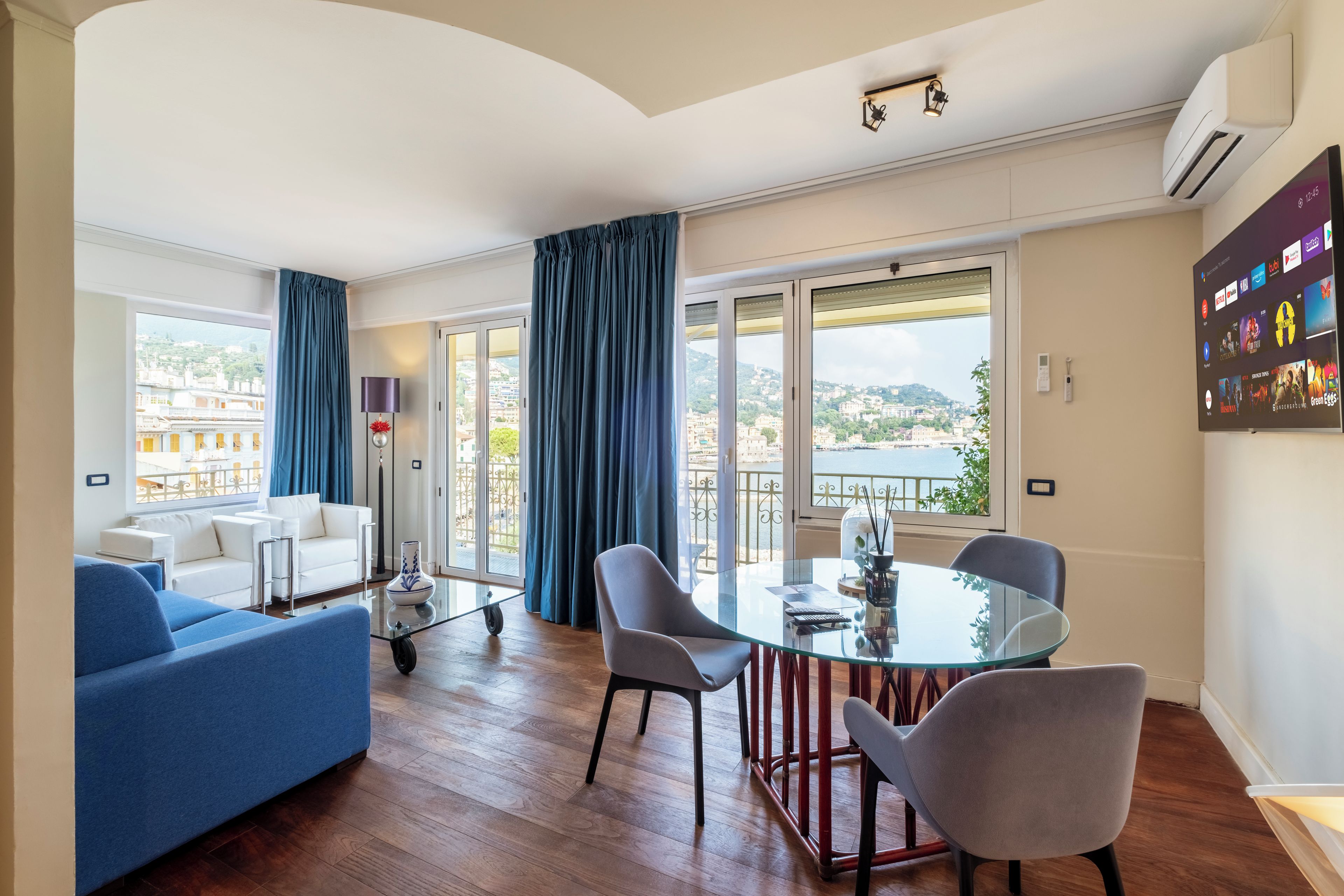 Un salon moderne avec une table à manger en verre, des chaises grises, un canapé bleu et un divan blanc.
