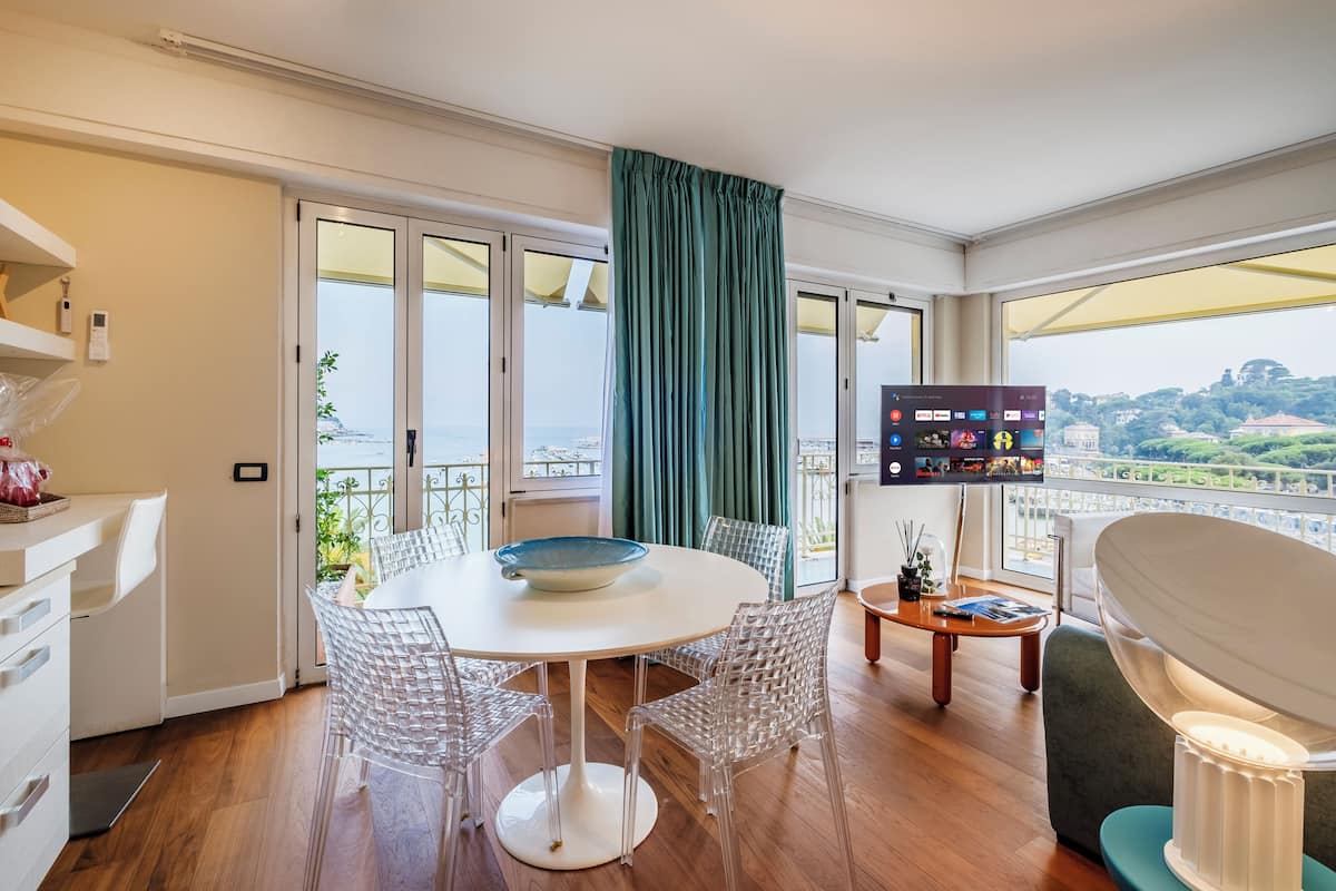 A modern dining area with a round table, clear chairs, and a view of the city through large windows.
