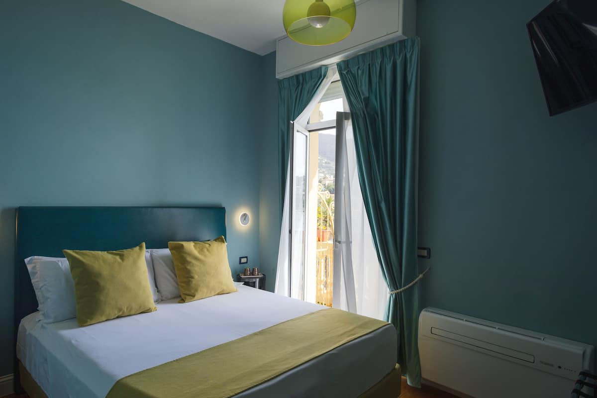 A bedroom with a bed, a nightstand, a window with curtains, and a wall-mounted light fixture.