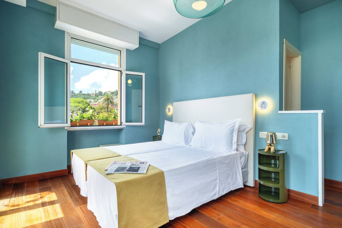 A bedroom with a large bed, a window with a view, a bedside table, and a nightstand.