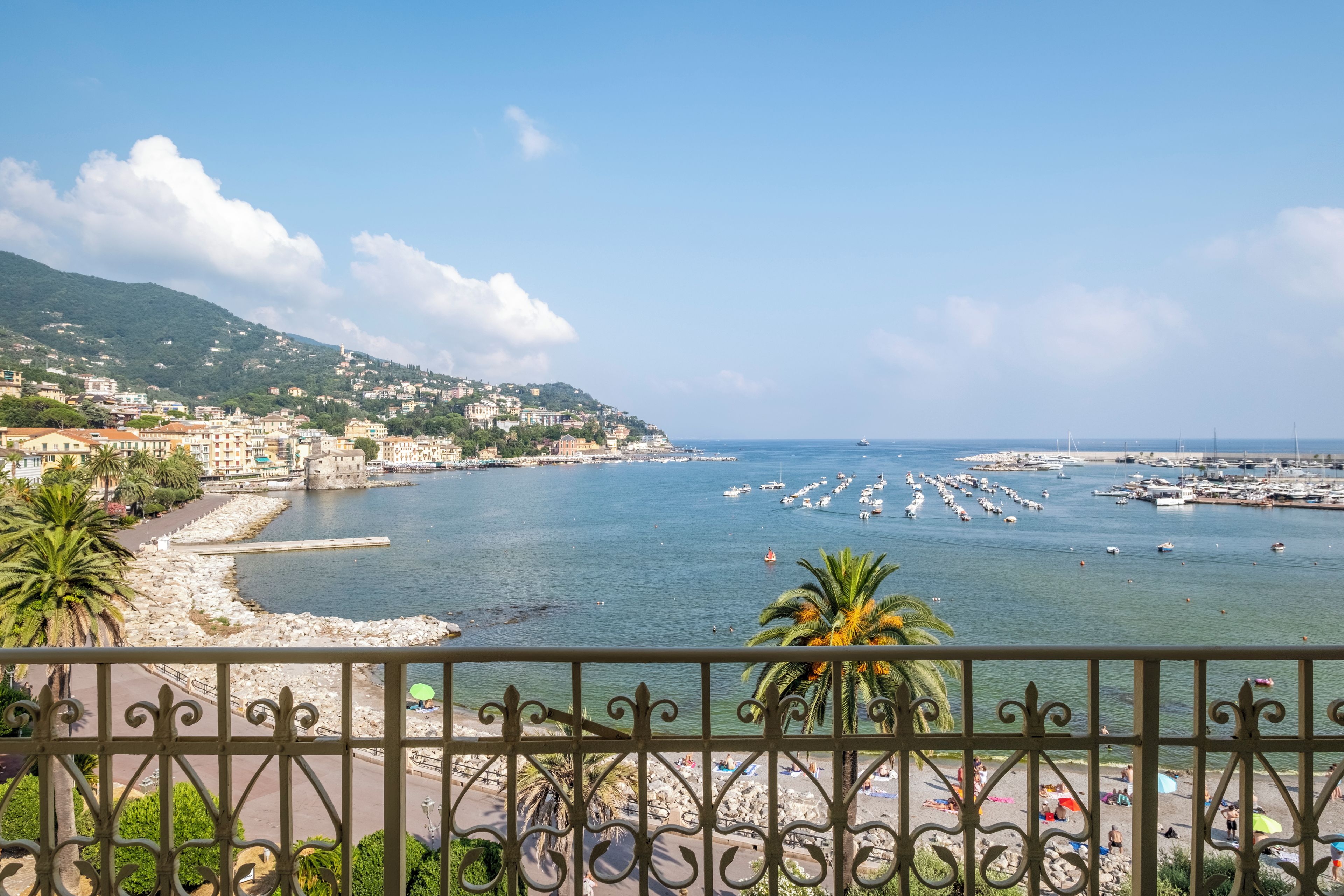 A coastal town with a marina, buildings along the hillside, and a beach with people.