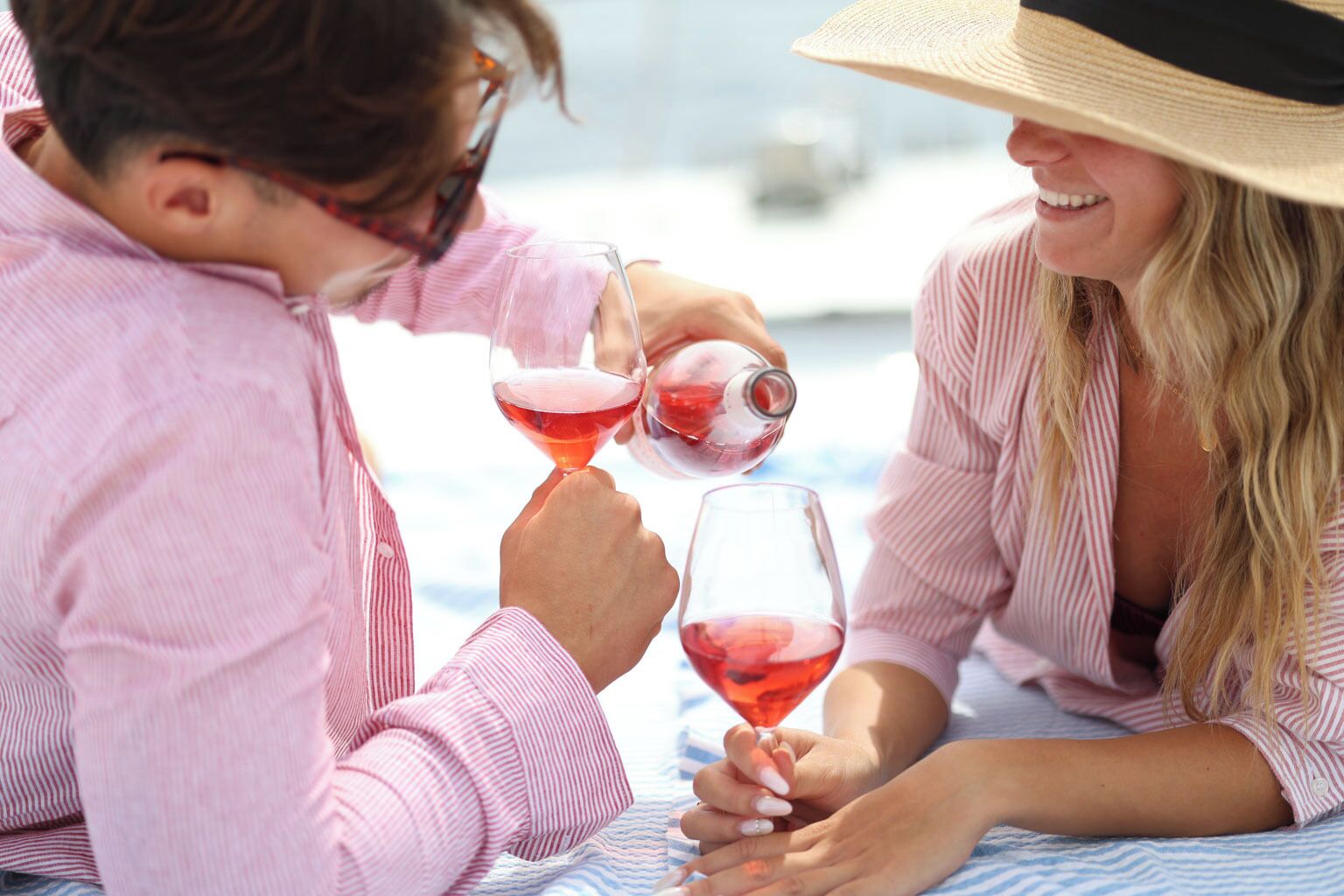 Two people sitting at a table with wine glasses, one pouring wine into the other's glass.