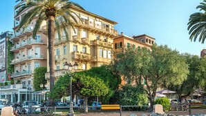 A multi-story building with balconies, a palm tree, and a rocky foreground. - Rosabianca Boutique Hotel (Rapallo)