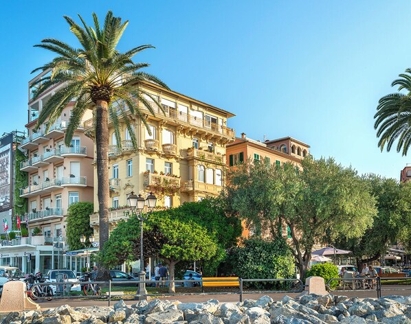 A multi-story building with balconies, a palm tree, and a rocky foreground. - Rosabianca Boutique Hotel (Rapallo)