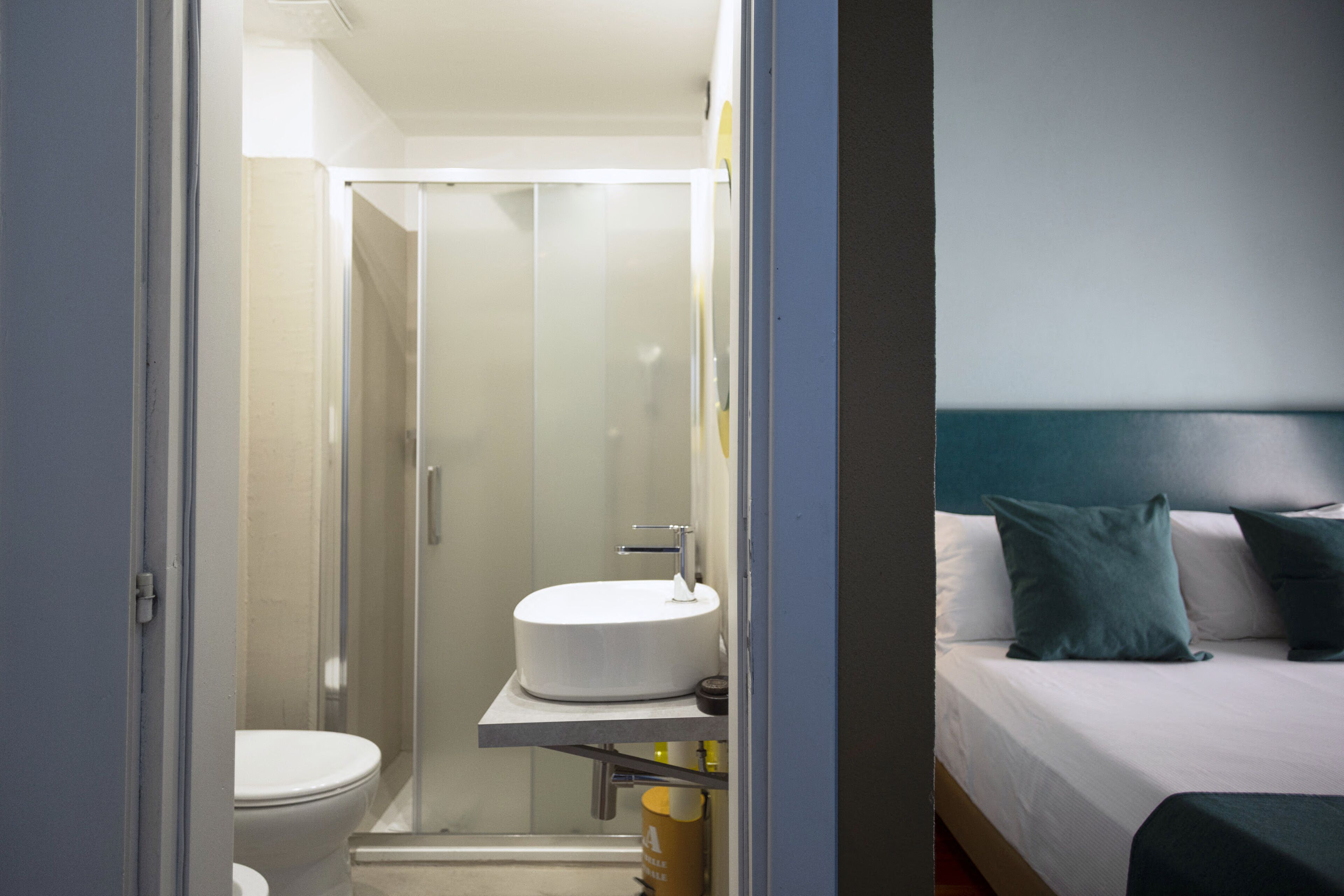 Un baño con inodoro, ducha con mampara de vidrio y lavamanos sobre una estantería.