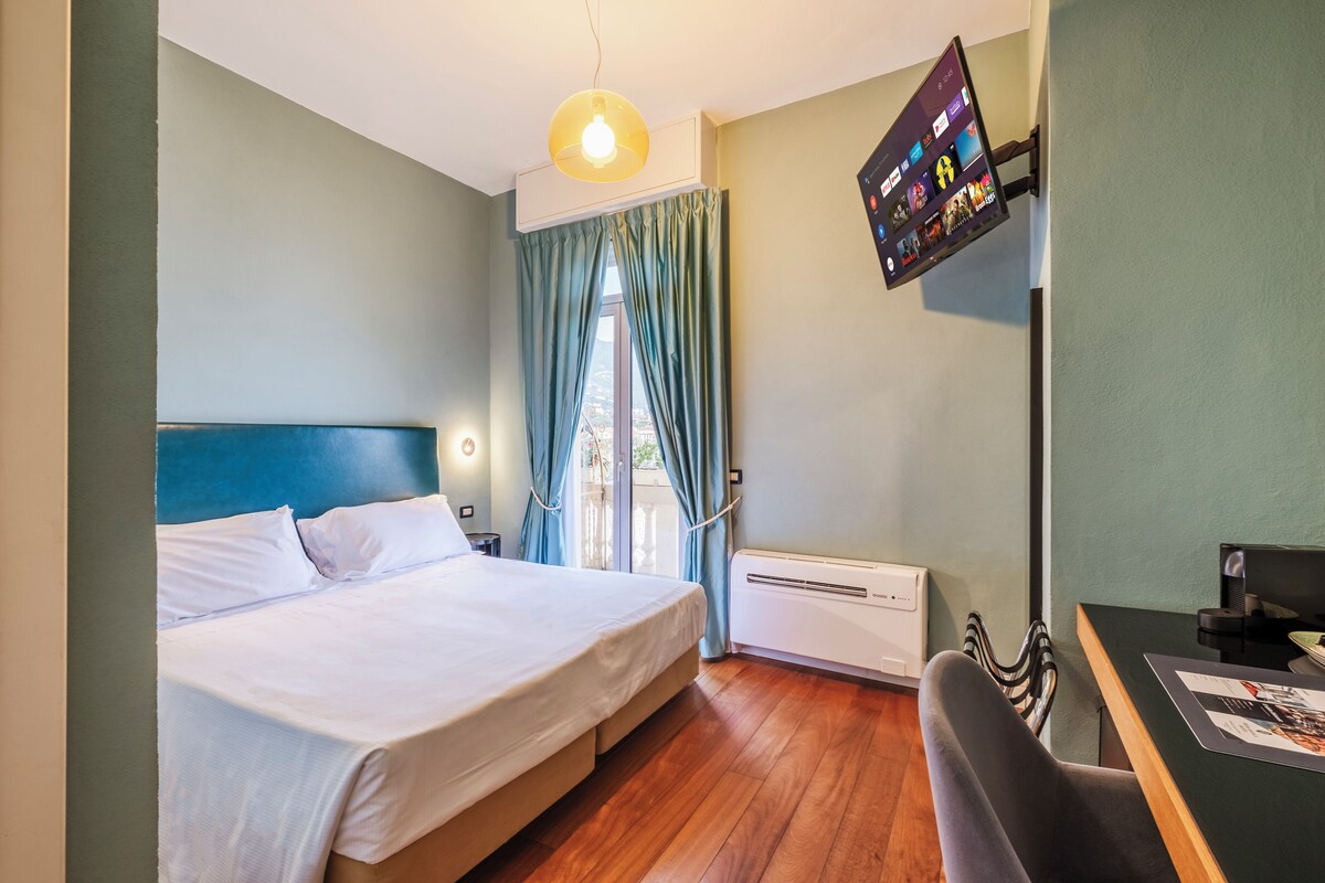 Una habitación de hotel con una cama, un escritorio, un televisor montado en la pared y una ventana con cortinas.