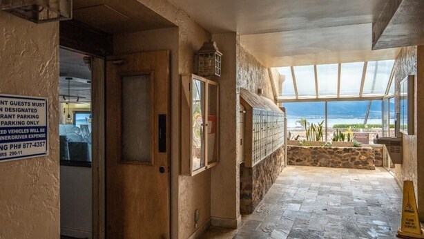A restaurant with a view of the beach, a stone wall, and a sign indicating designated parking. - Menehune Shores #423 2 Bedroom Condo by RedAwning (Kihei)